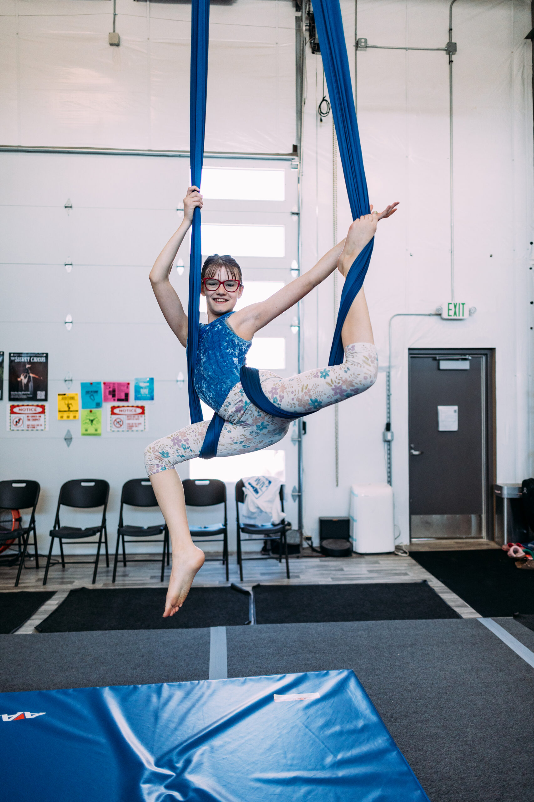 A teen student in an aerial silk doing a stag pose. She is in a beginner dance class for teens at aerial cirque over denver.