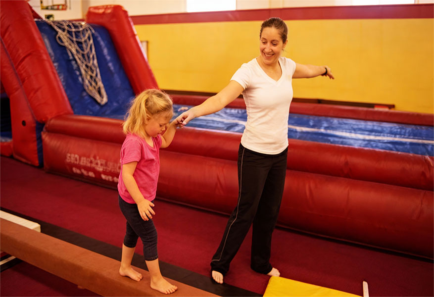 ACOD_gymnastics-instructor-helping-toddler-walk-balance--AerialCirqueOverDenver