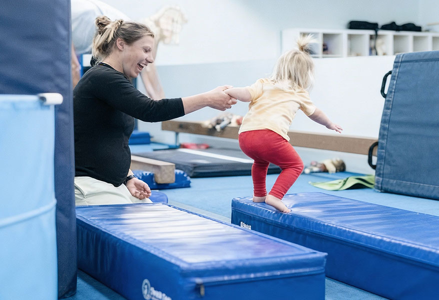 ACOD_gymnastics-instructor-helping-toddler-walk-mats--AerialCirqueOverDenver