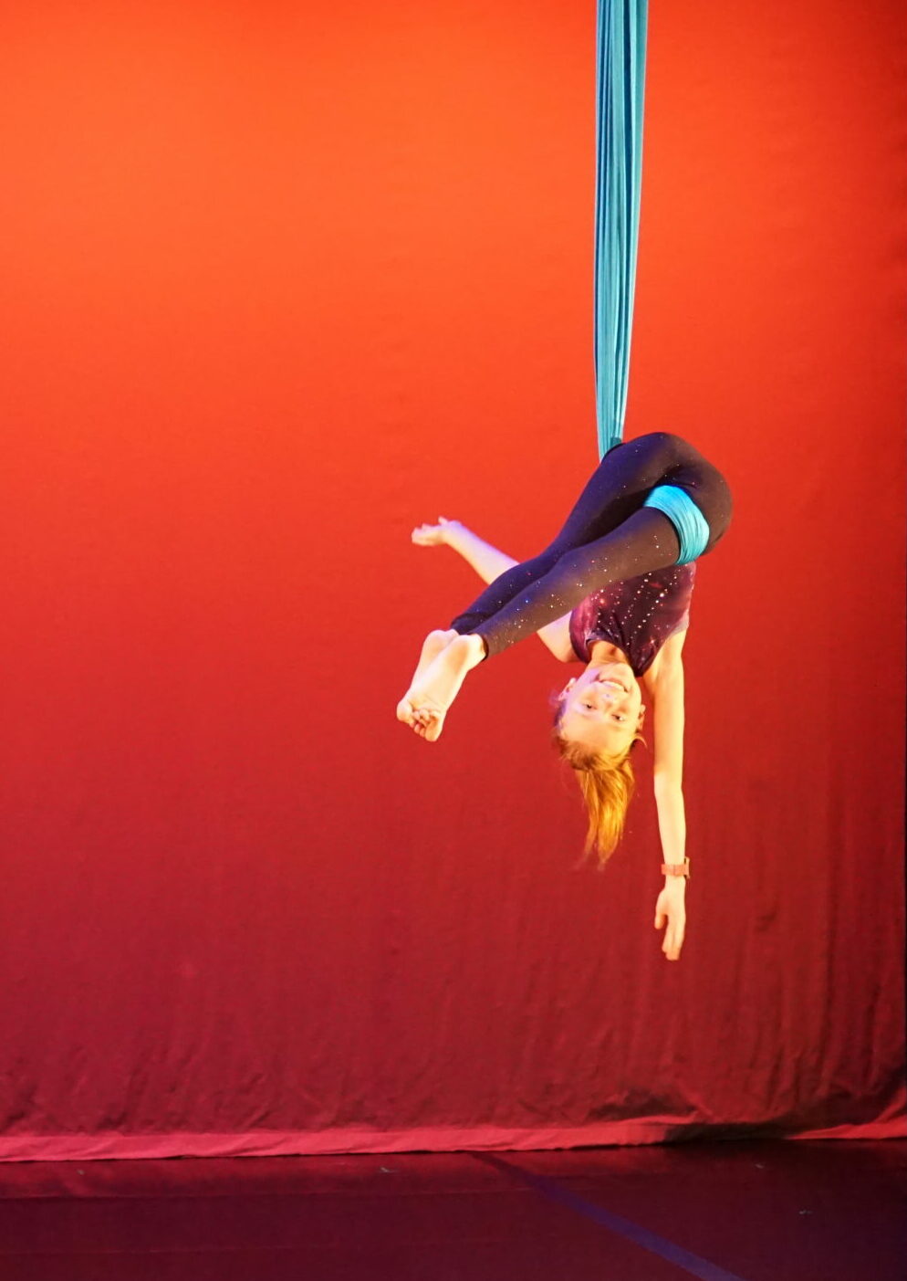 young dancer on an aerial sling smiling for the camera. She is performing at an aerial dance performance showcase