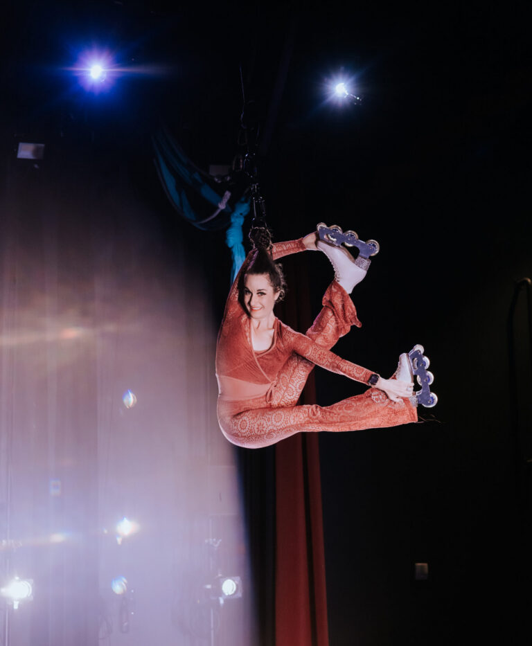 Aerial hair hanger with roller skates in a flexible split position while suspended in the air from her hair