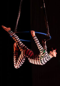 An aerialist on a tippy lyra does a performance at a show with a black background
