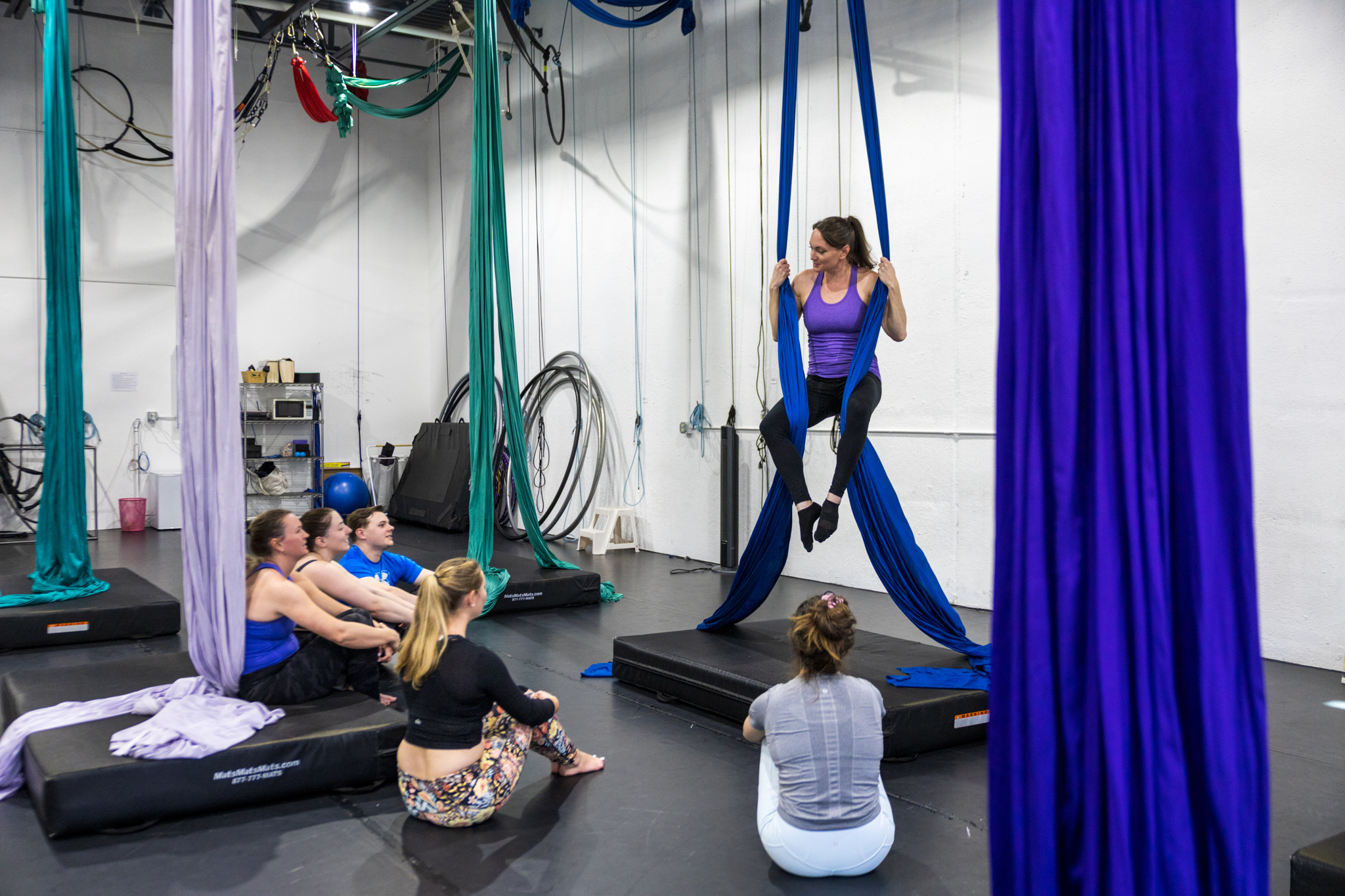 aerial dance instructor teaching adult student group. Instructor is demonstrating a beginner level move for adult dancers.