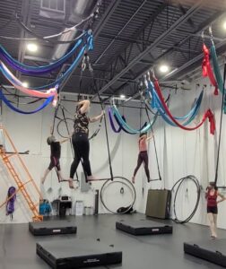 adult dance classes in denver, students work a beginner trick on aerial trapeze